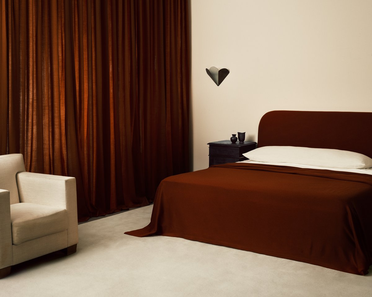 Ein Schlafzimmer mit dem Teppich Grand in Dusty White, kombiniert mit Vorhängen in einem Ton von Burnt Red.