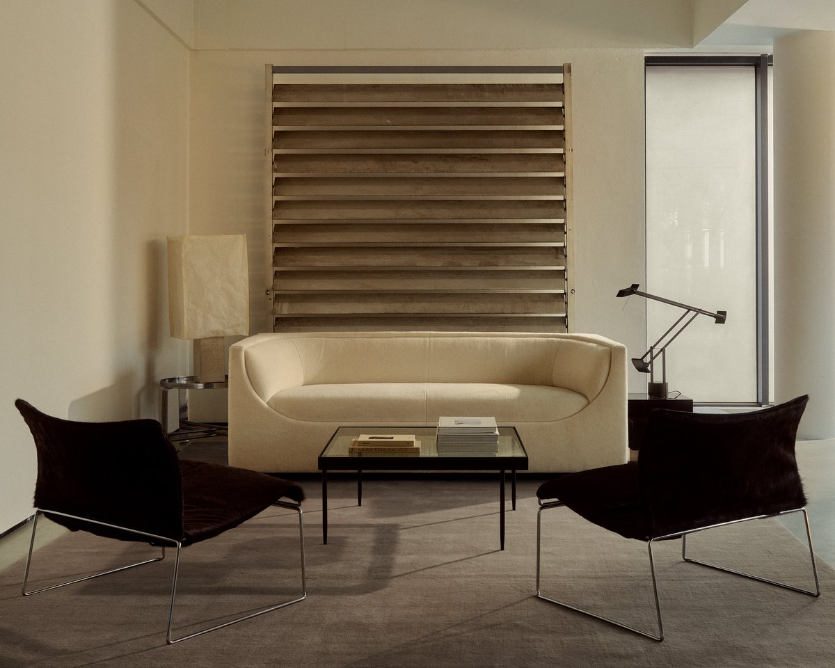 Mattan Grand i färgen Warm Gray, visad med moderna möbler såsom en krämfärgad soffa och två svarta fåtöljer med metallram.