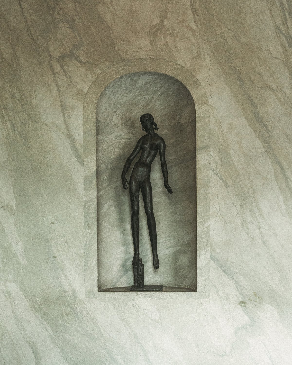 A slender bronze sculpture displayed in a marble wall niche at Stockholm Concert Hall.