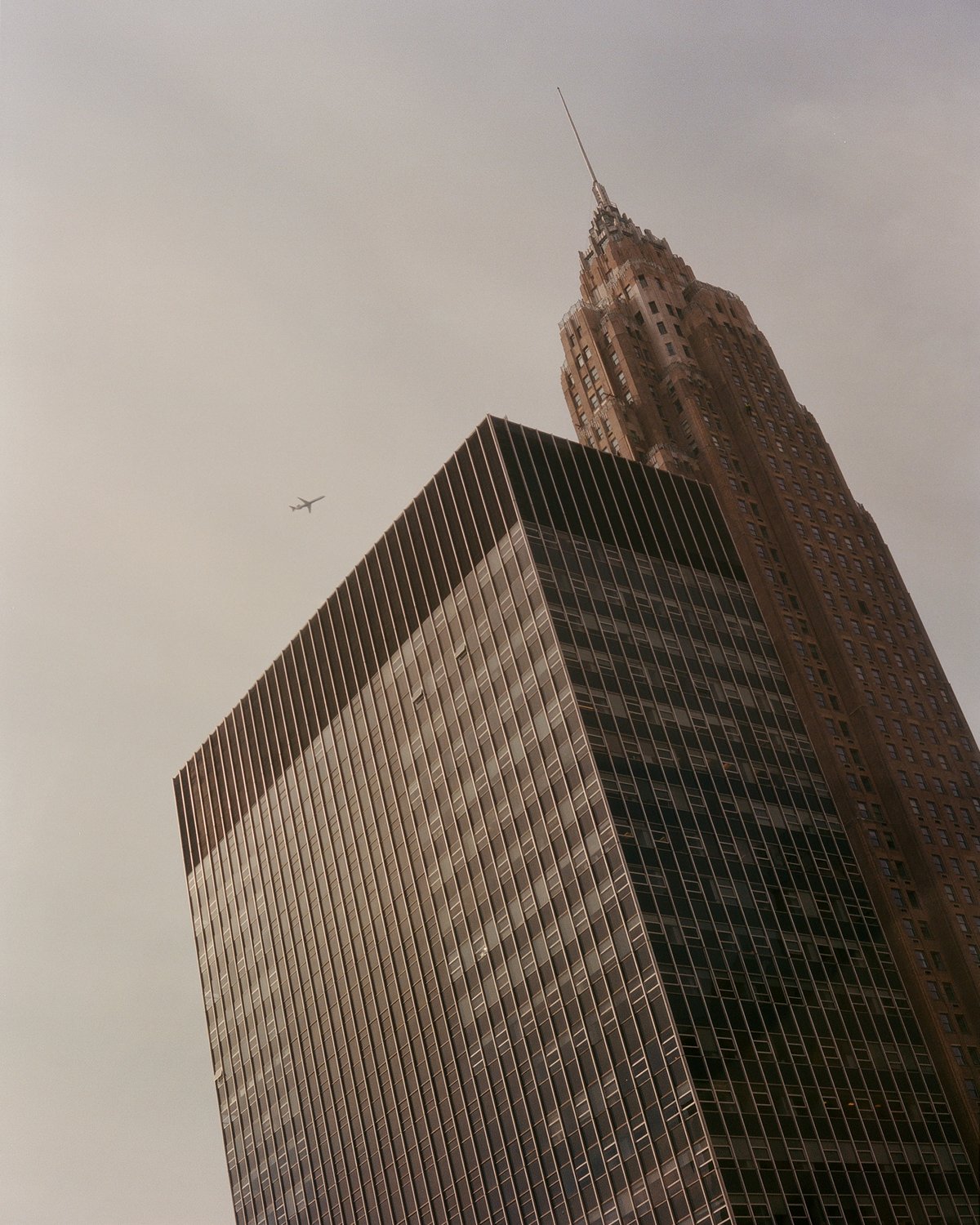 Ein Hochhaus in New York, von unten aufgenommen, während ein Flugzeug vorbeifliegt.