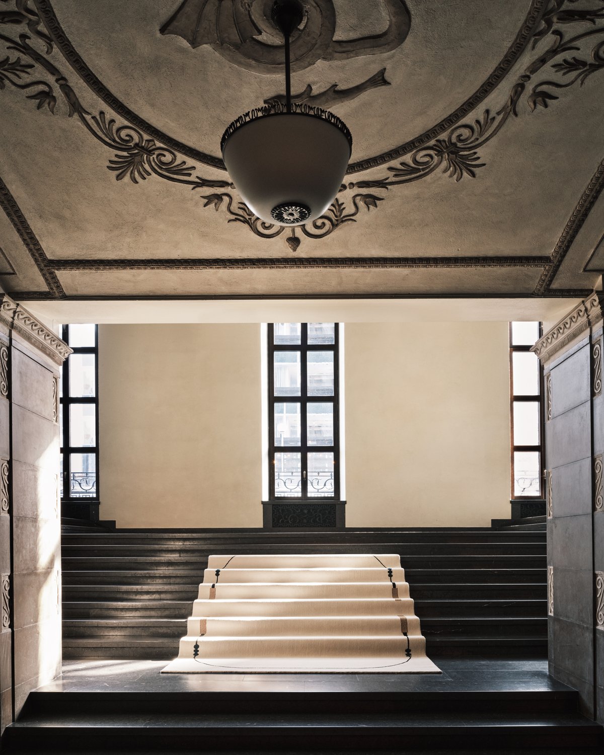 Grace 02 – Tassel — displayed on the grand staircase of Stockholm Concert Hall. The handwoven cream rug features curved black lines and tassel motifs in a balanced, symmetrical composition.