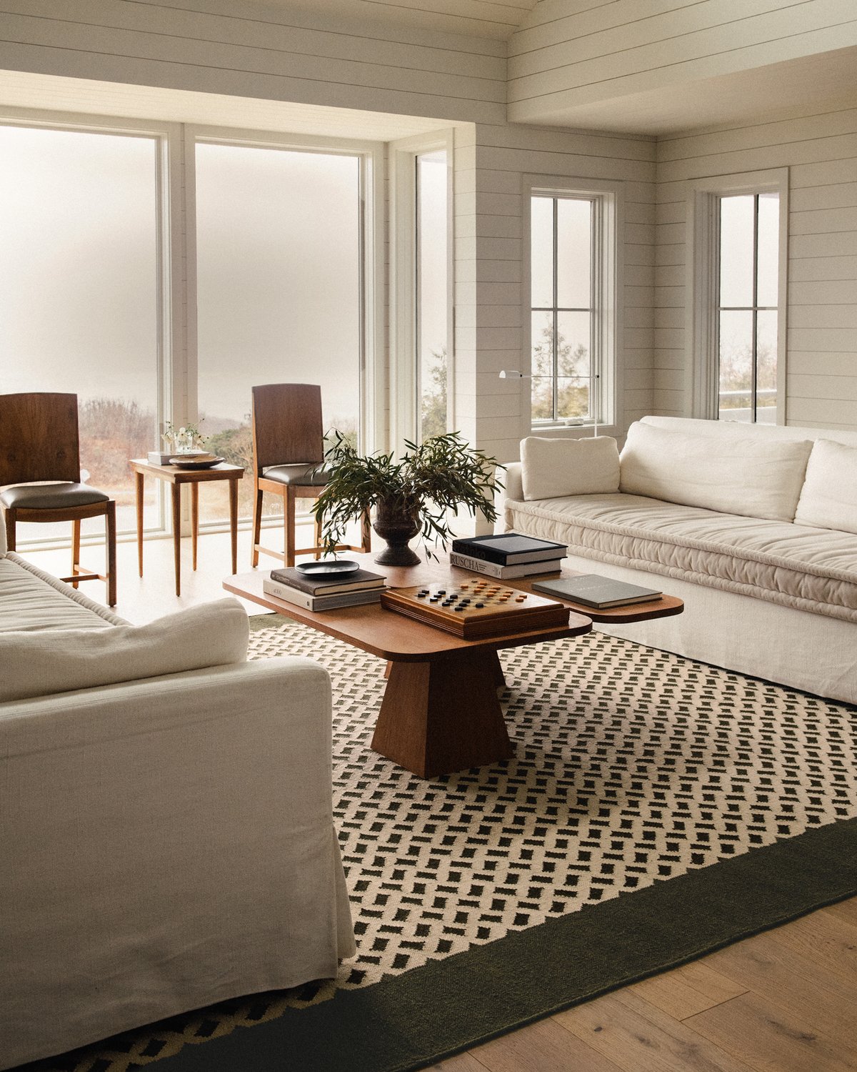 Orleans rug displayed in a bright living room, alongside two cream-coloured sofas and an asymmetric coffee table.