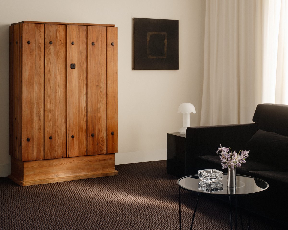 Harvest Wall-to-Wall carpet in Rye, styled in a room with a wooden cabinet and black sofa, showing its structured jacquard weave in a deep, warm brown tone.