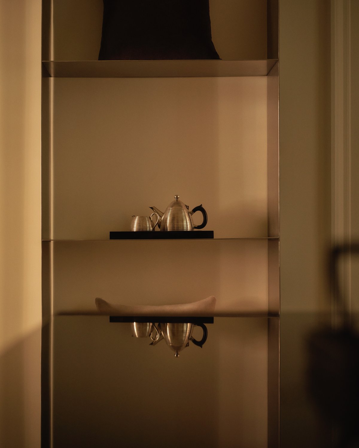 A detail from the Nordic Knots store on Mount Street in London, showing a softly lit shelving unit with silver teapots and minimal decor, creating a warm and refined atmosphere.