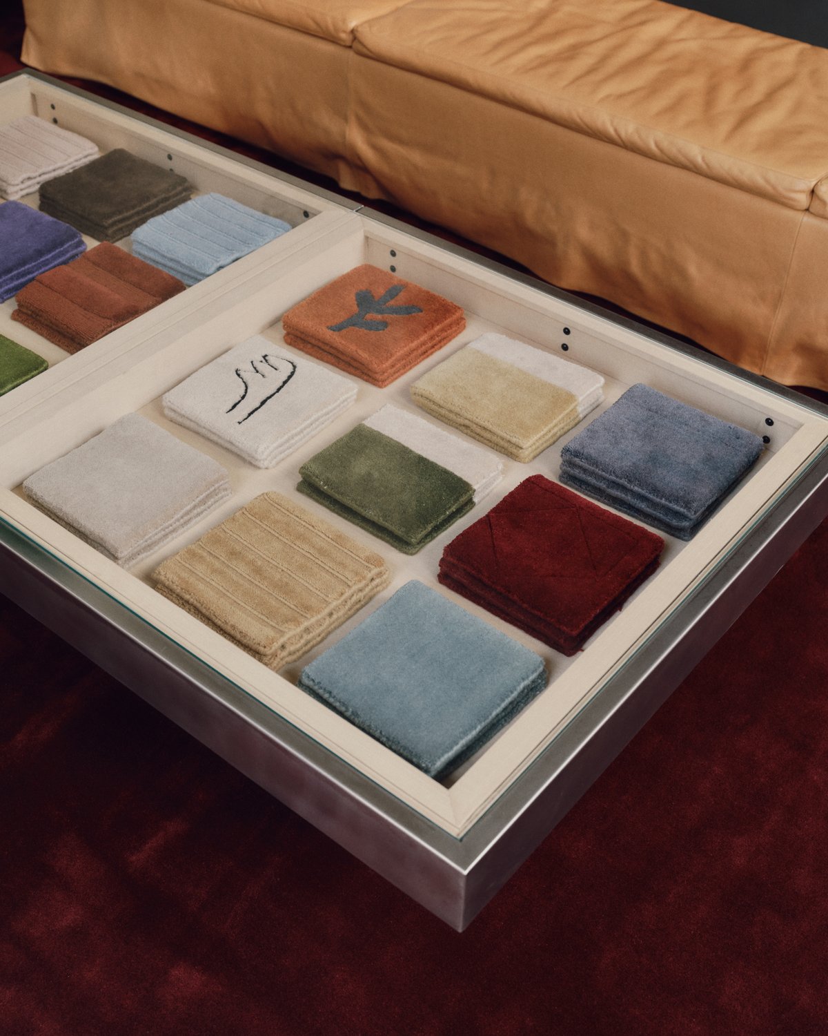 Teppichmuster in verschiedenen Farben und Texturen, ordentlich in einer Edelstahlschublade neben einer Lederbank angeordnet.