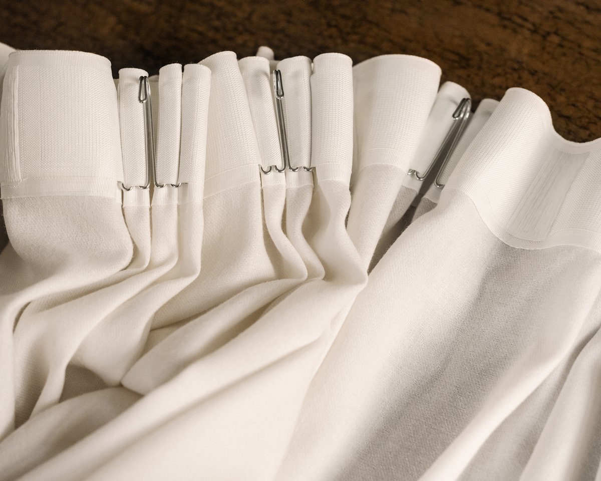 Rideaux The Grand en Perfect White présentés en gros plan, mettant en valeur leurs plis structurés, leur texture raffinée et leur finition soignée.