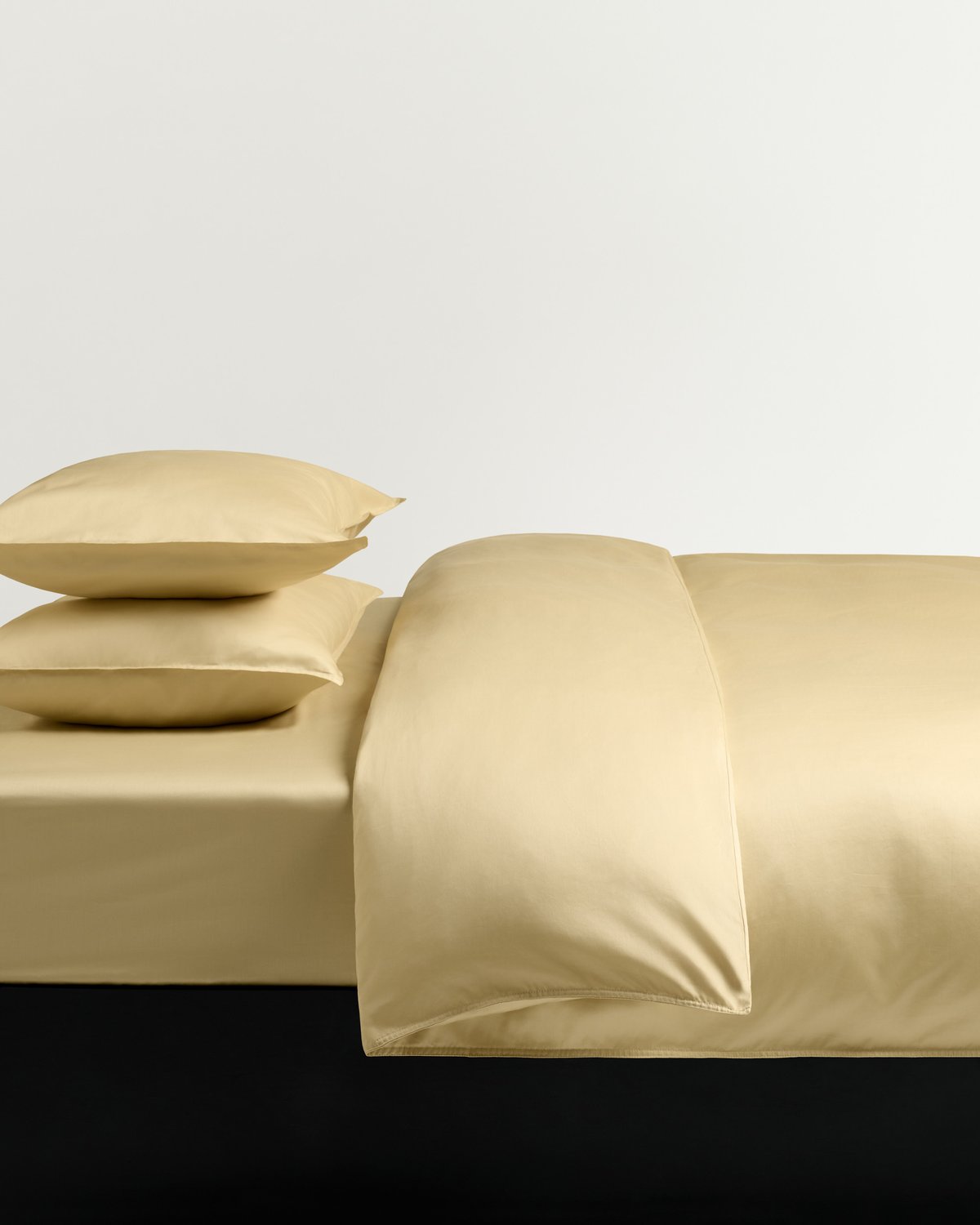 A made bed dressed in soft yellow cotton sateen with a smooth, lustrous finish against a light background.