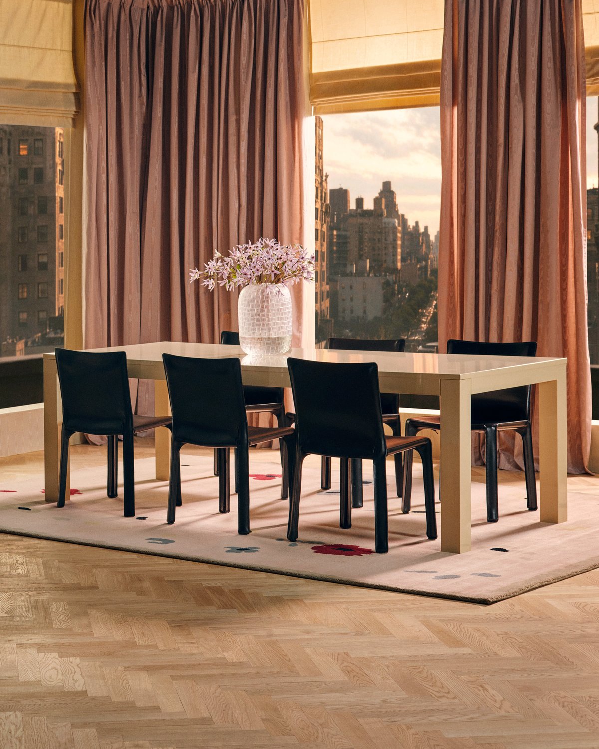 Belmont in Old Rose, a rug with scattered flowers, beneath a dining table with black chairs and tall pink moiré curtains.