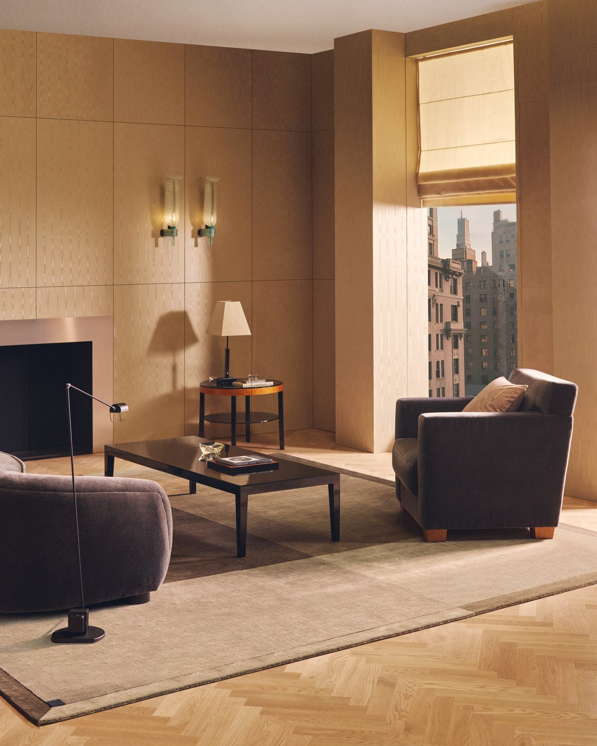 Parchment in Sand, a rug with a tonal border, in a room with grey velvet seating and a view over the city.