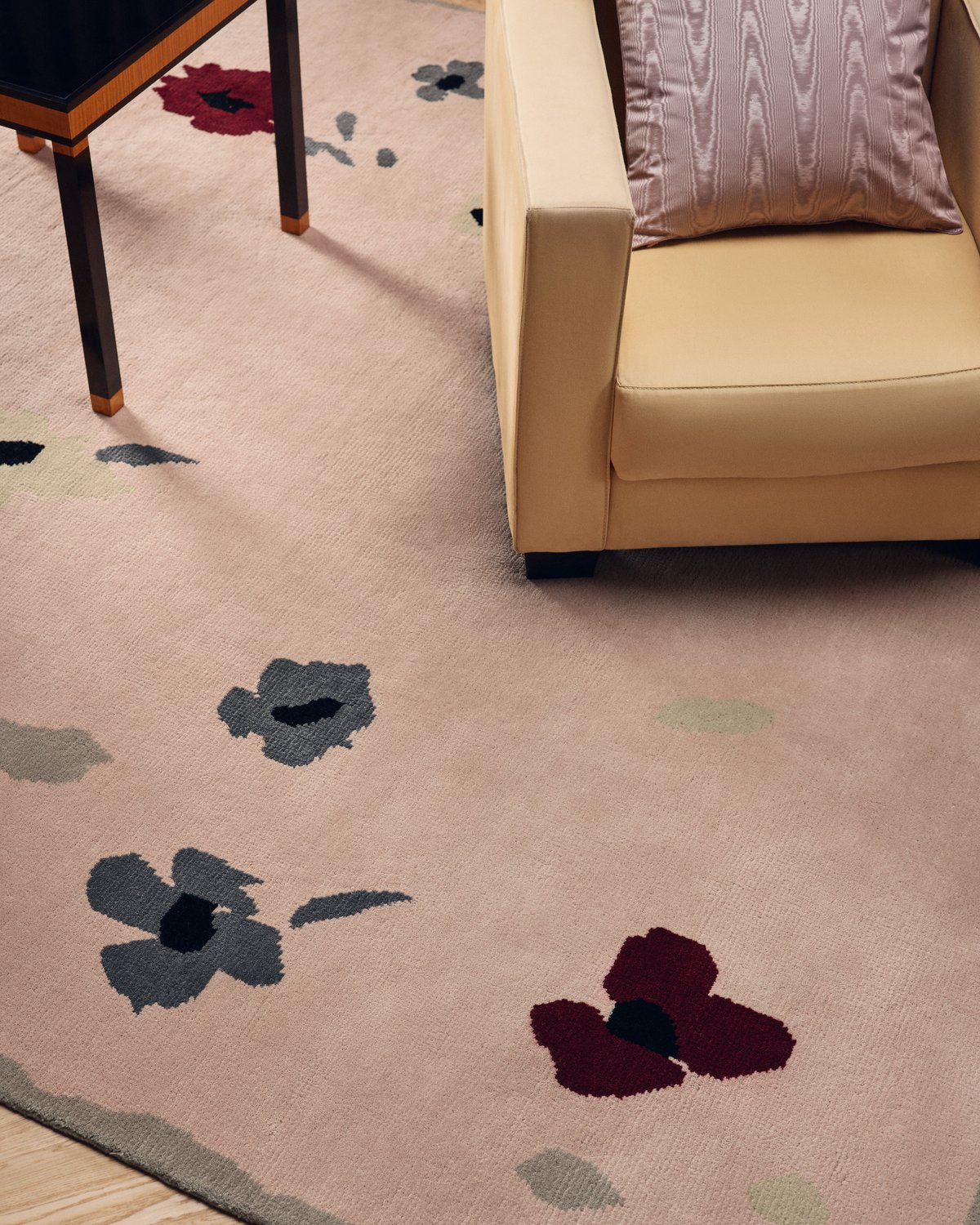 Close-up of Belmont in Old Rose, a rug with scattered grey and burgundy flowers, beneath a yellow armchair.
