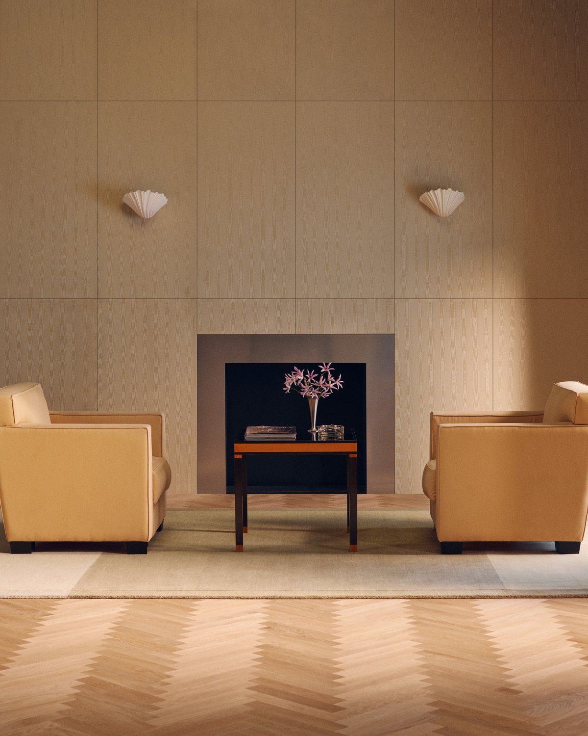Parchment in Sand, a rug with a tonal border, beneath two yellow armchairs in front of a steel fireplace.