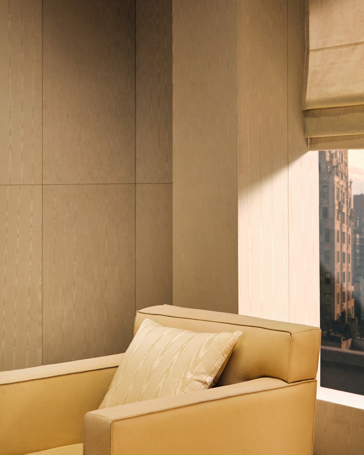 Moiré Cushion Cover in Sand on a yellow armchair, by a window with a pale Roman Blind.