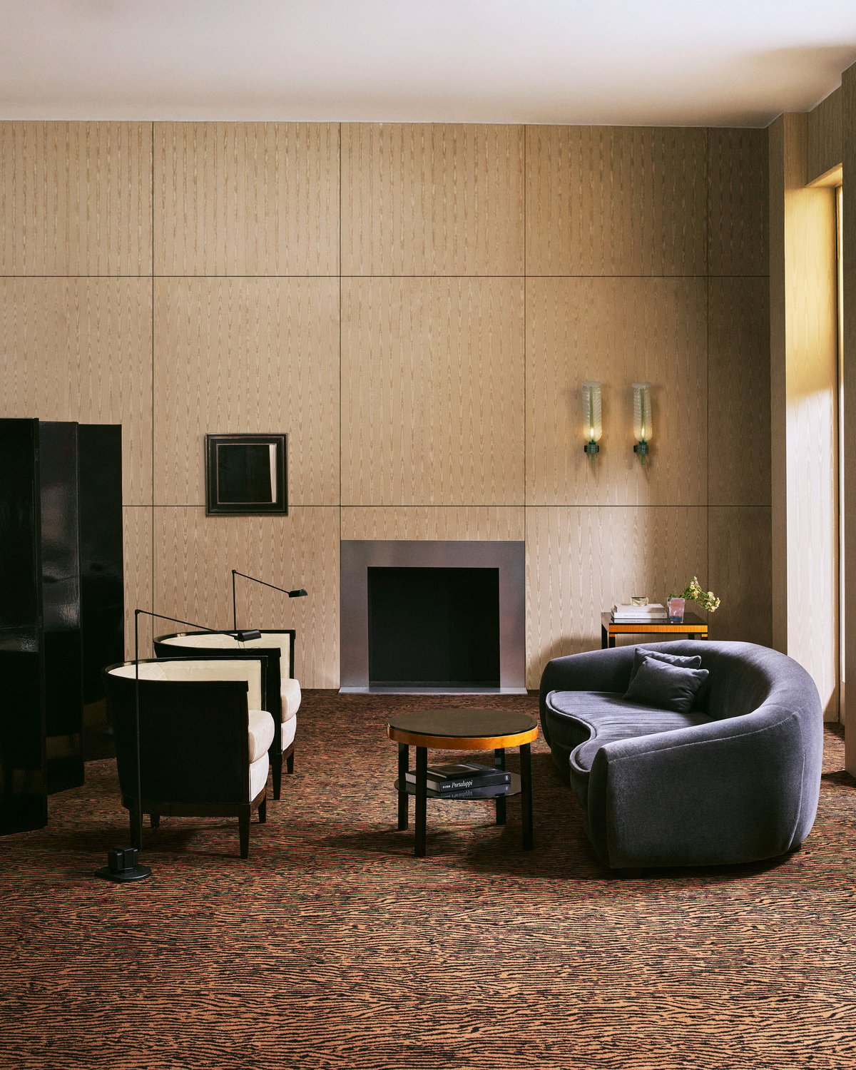A wall-to-wall carpet with a black and camel tiger stripe, in a room with a curved grey velvet sofa and a black lacquered screen.