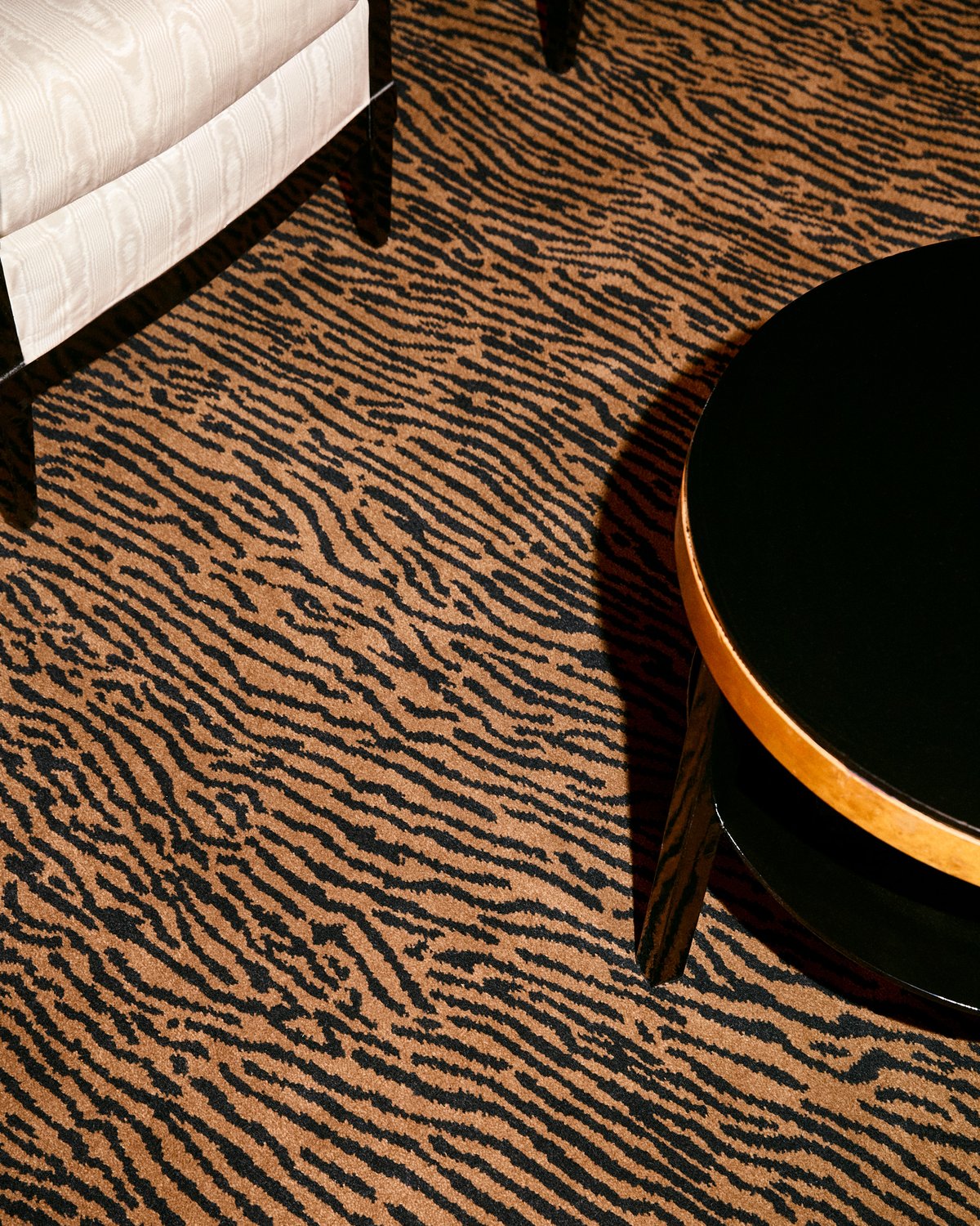 Close-up of a black and camel tiger-stripe carpet beneath a cream armchair and a round black table.