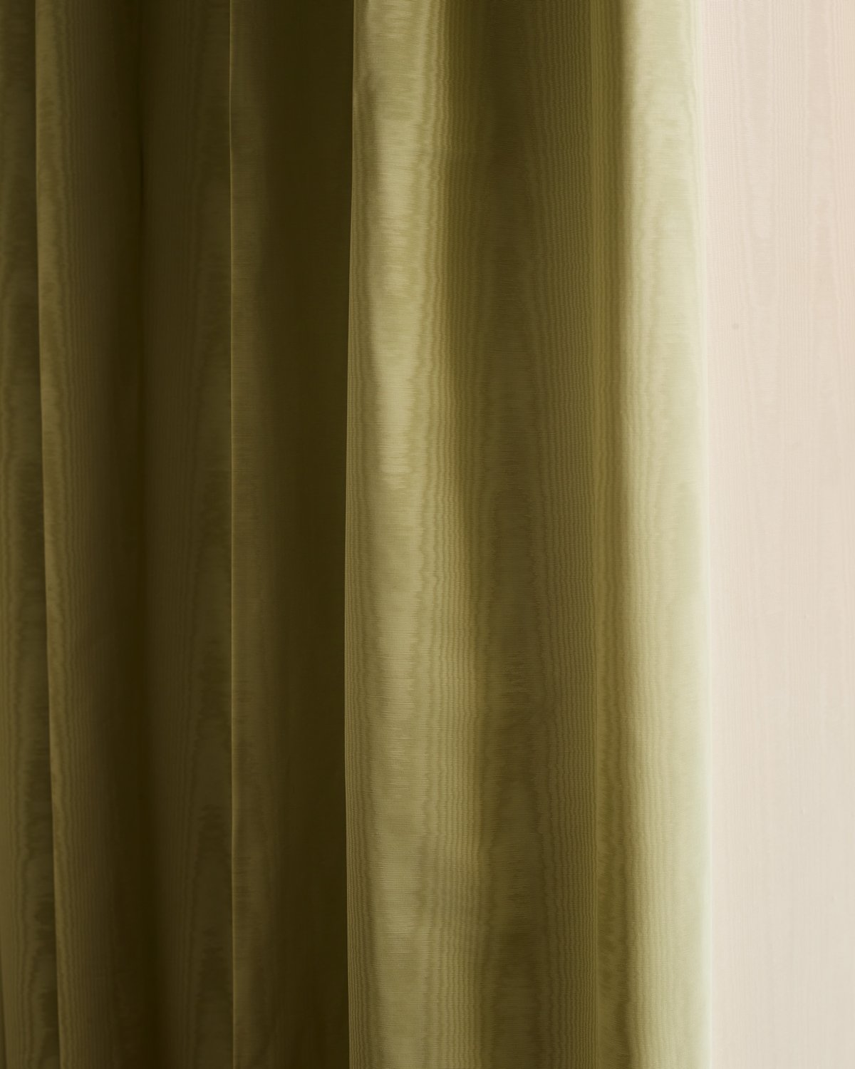 Close-up of an olive green moiré curtain hanging in soft folds against a pale wall.