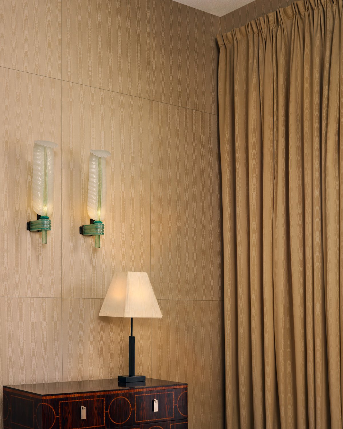 A golden moiré curtain hanging in soft folds beside matching moiré wall panels and two glass wall lights.
