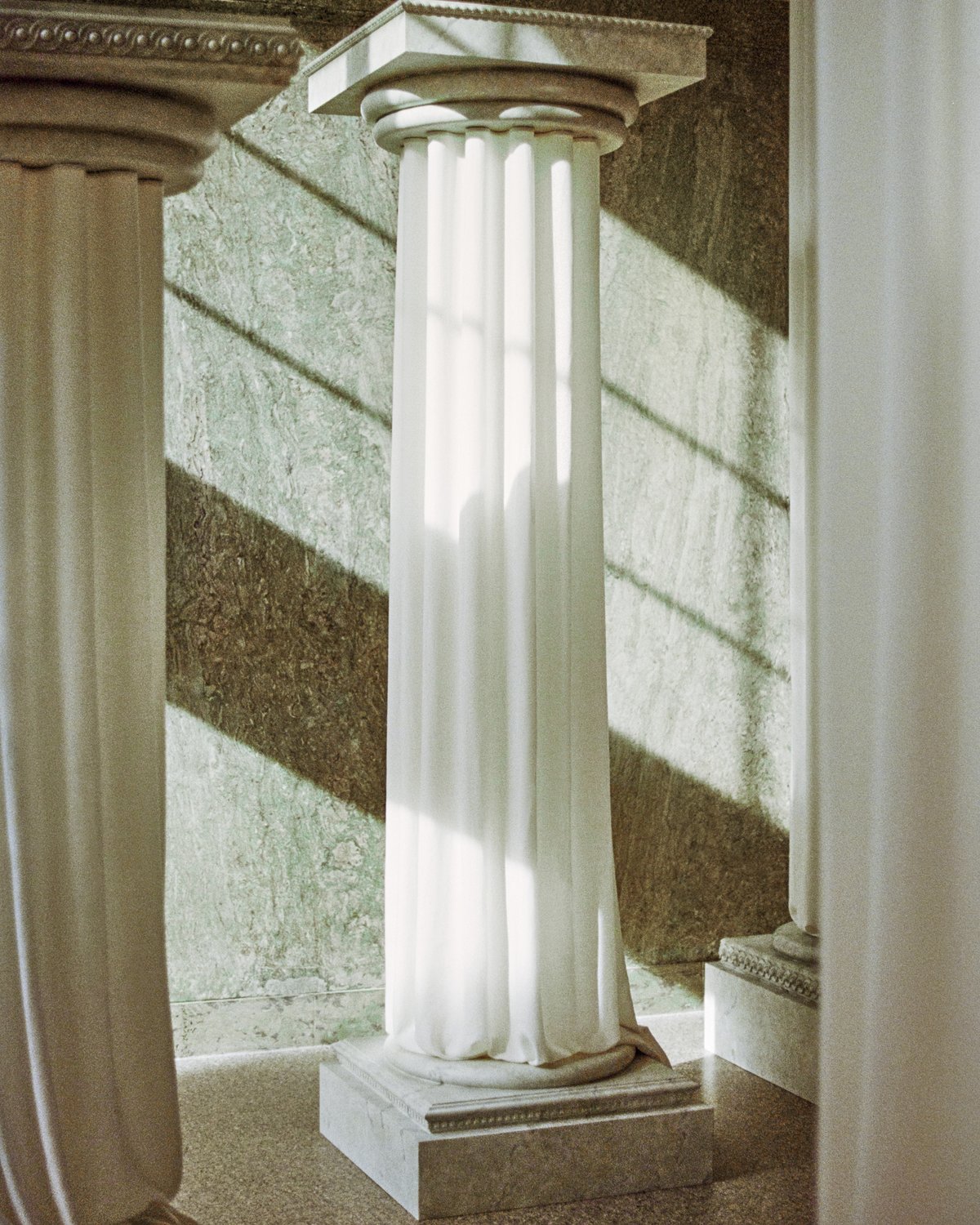 The Grand curtains on an ancient greek style pillar in the Stockholm Flagship with the light shining in through the windows onto the green marble interior.