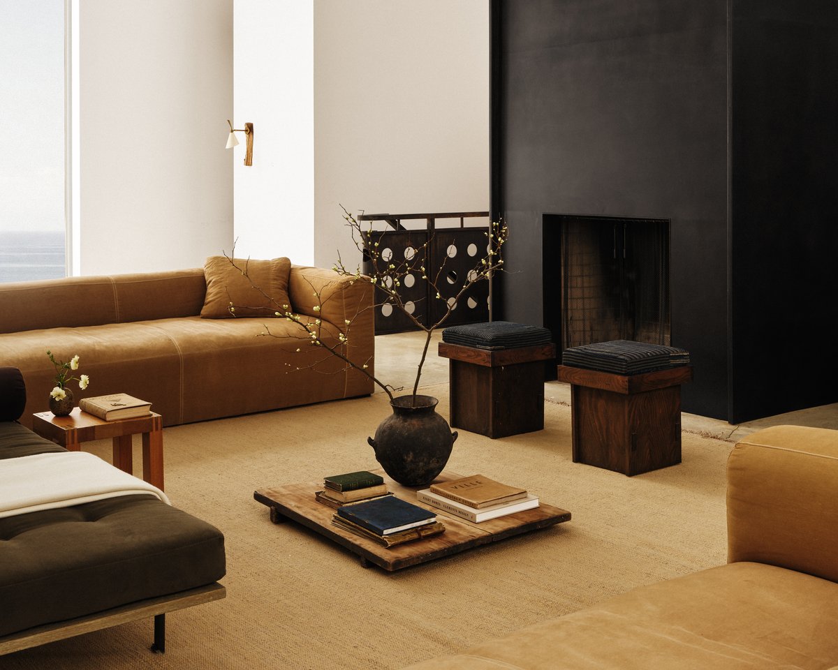 Desert rug in Straw — a flatweave rug in a light straw tone with a subtle woven texture, styled in a living room with a black fireplace and warm-toned seating.