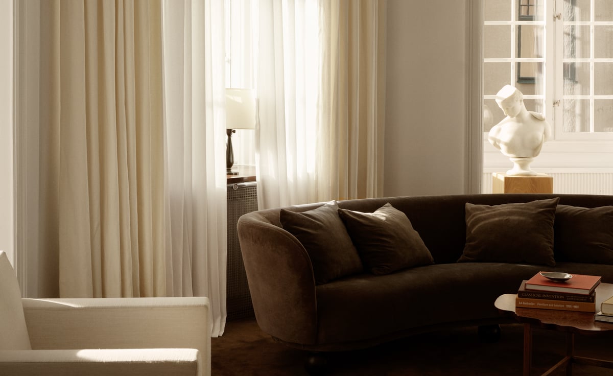 The Shade curtain in Warm White layered with The Sheer curtain in Perfect White — a double-layer window treatment combining a softly textured, opaque fabric with a light, airy sheer, both falling in gentle vertical folds in warm white tones.