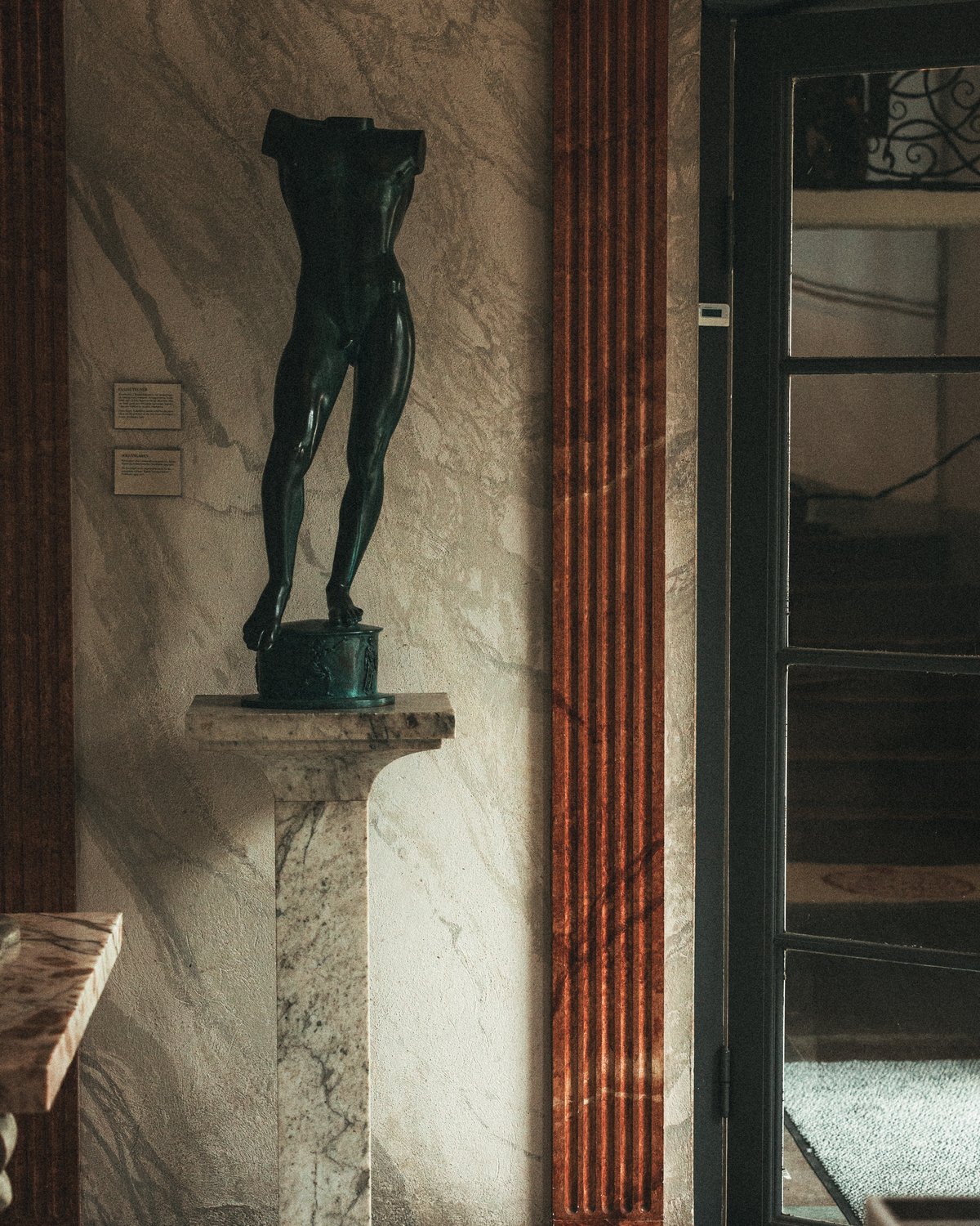 A headless bronze torso sculpture displayed on a marble pedestal inside Stockholm Concert Hall.