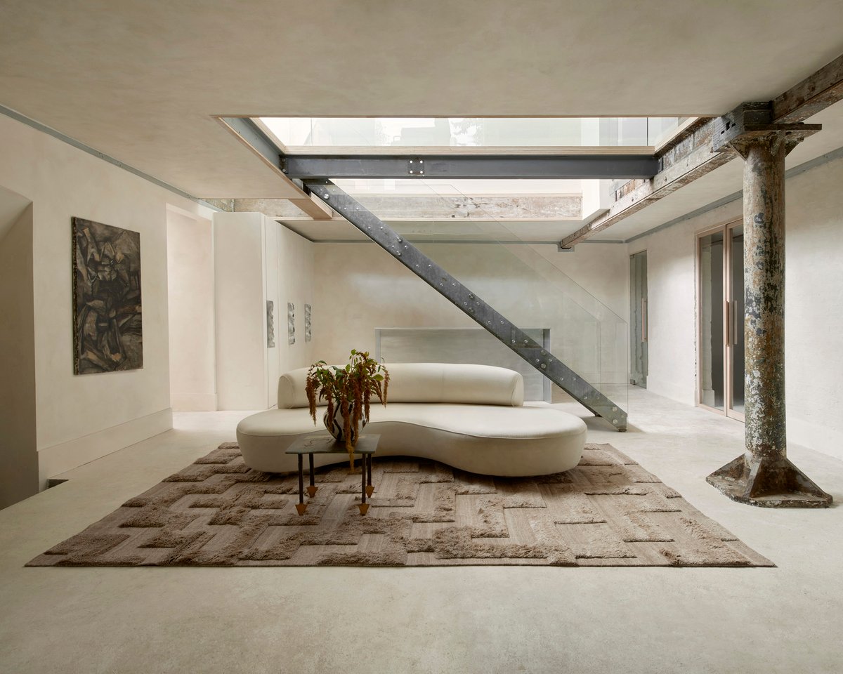 Boho Rug in Brown adds rich texture and depth to a minimalist loft, pairing its tonal pattern with raw beams, concrete floors, and a sculptural cream sofa.