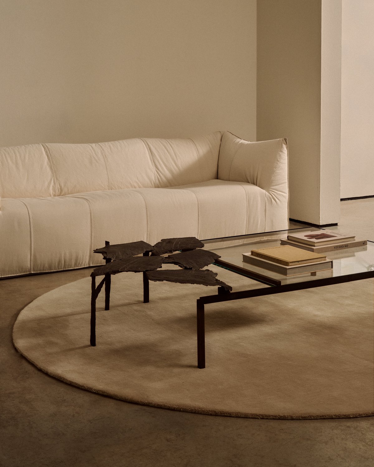 Mattan Grand Round i färgen Sand, placerad under ett soffbord i metall och glas som skapar en vacker struktur.