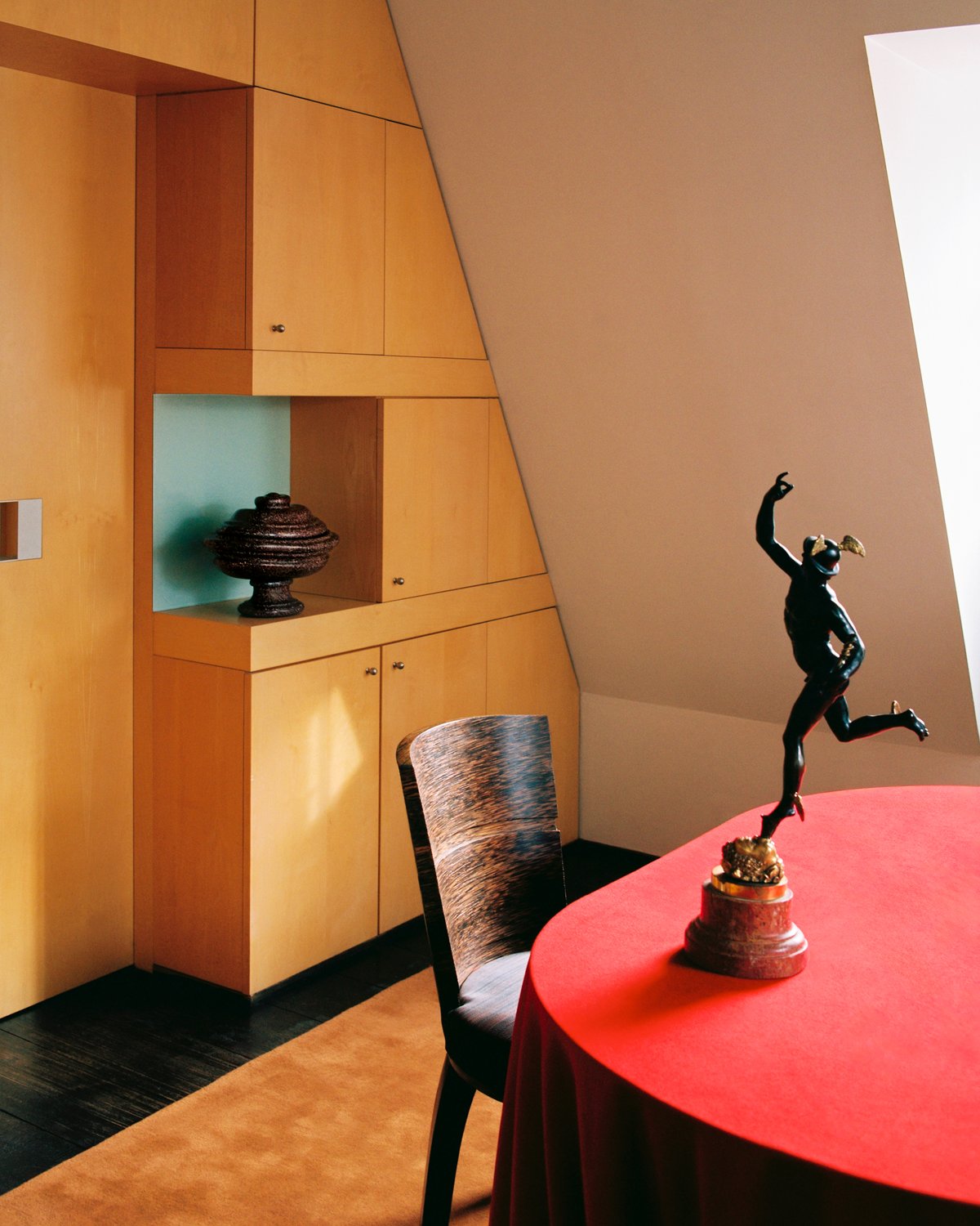 Grand in Pecan, photographed in warm light beneath a dining table with a red tablecloth, set against pale wood cabinetry.