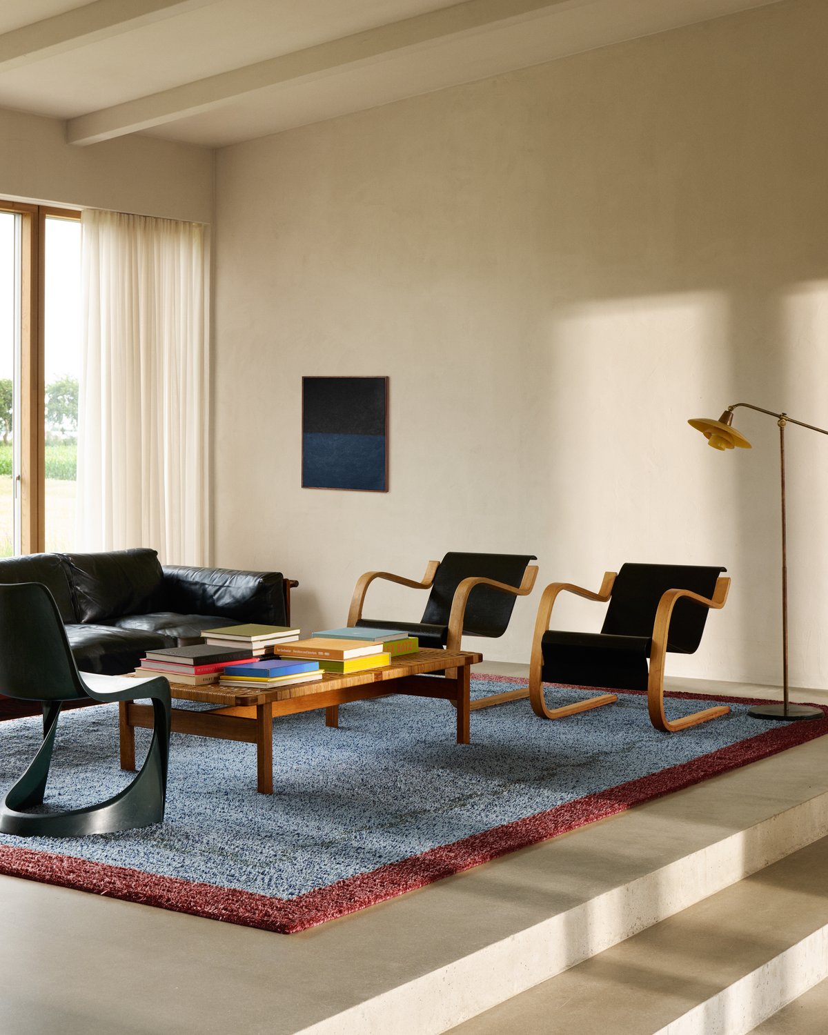 Tapis en laine à poils longs Ryya en Blue, photographié dans un salon moderne en Scanie, avec des meubles noirs et en bois.