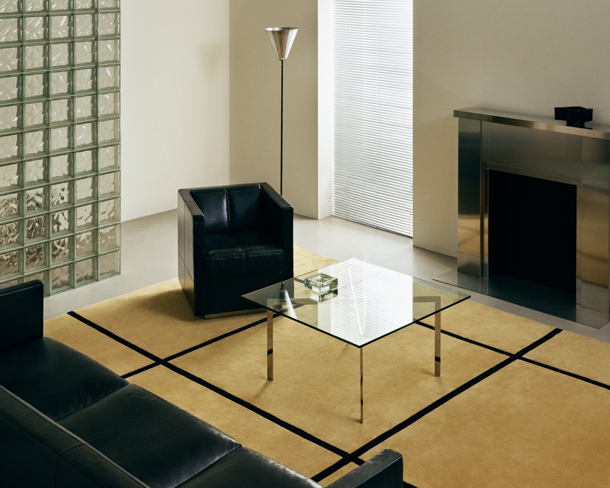 Plush wool rug Pavilion in Yellow pictured in a modern living room with a chrome fireplace, glass coffee table and black leather sofa.