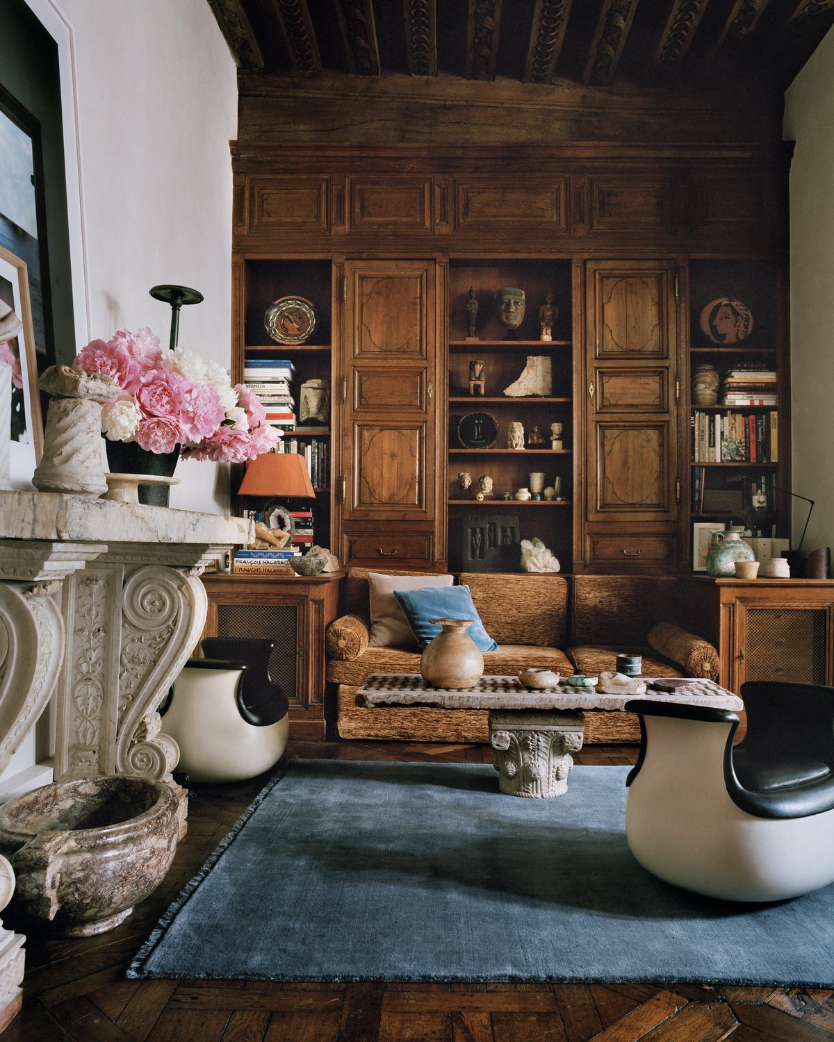 The Mohair rug in Slate Blue is shown in a Paris living room with wooden paneling, sculptural furniture, and a marble fireplace decorated with pink flowers, creating a rich and layered atmosphere.