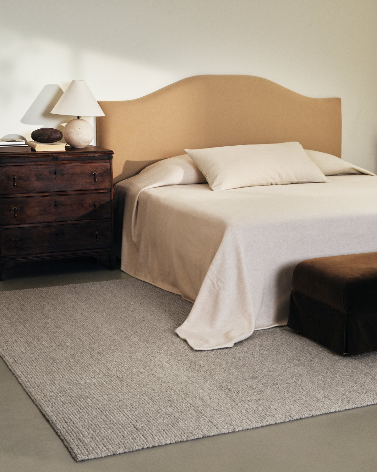 Flatweave wool rug Braid in Taupe Mix pictured in a bedroom with white bed sheets and a beige bed frame.