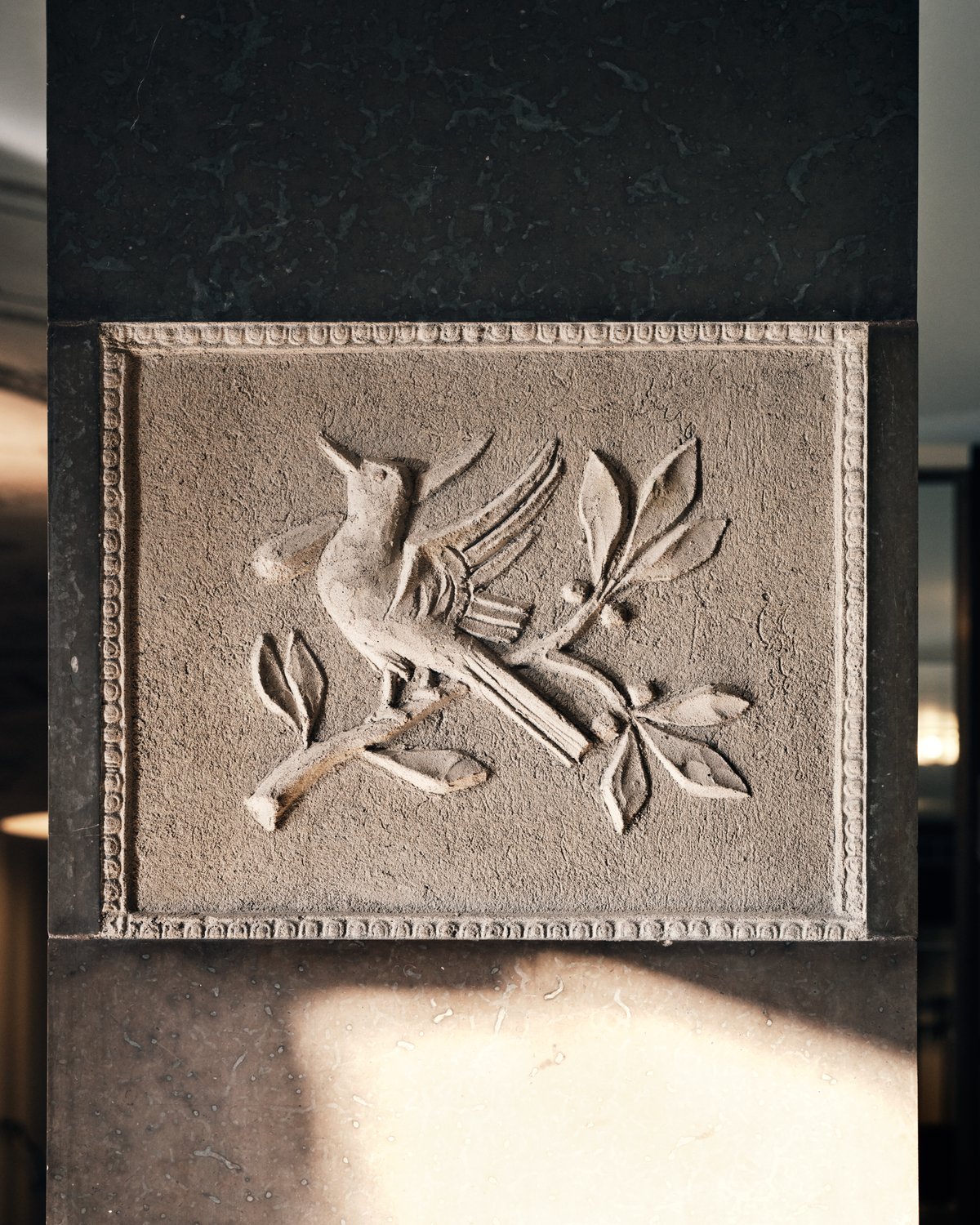 Ein in Stein gemeißeltes Relief zeigt einen Vogel auf einem Ast, umgeben von feinen Blättern, im Konzerthaus Stockholm.
