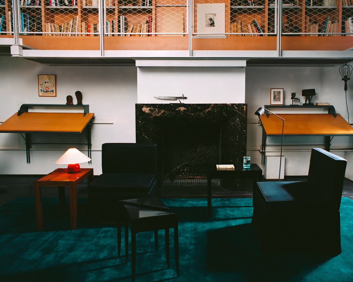 Grand in Emerald Green, photographed in a loft living space beneath black lounge chairs and low tables, with a fireplace and bookshelves in the background.