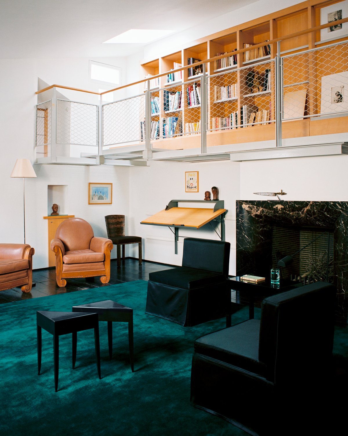 Grand in Emerald Green, photographed in a bright loft living room beneath black seating, with bookshelves and a fireplace in the background.