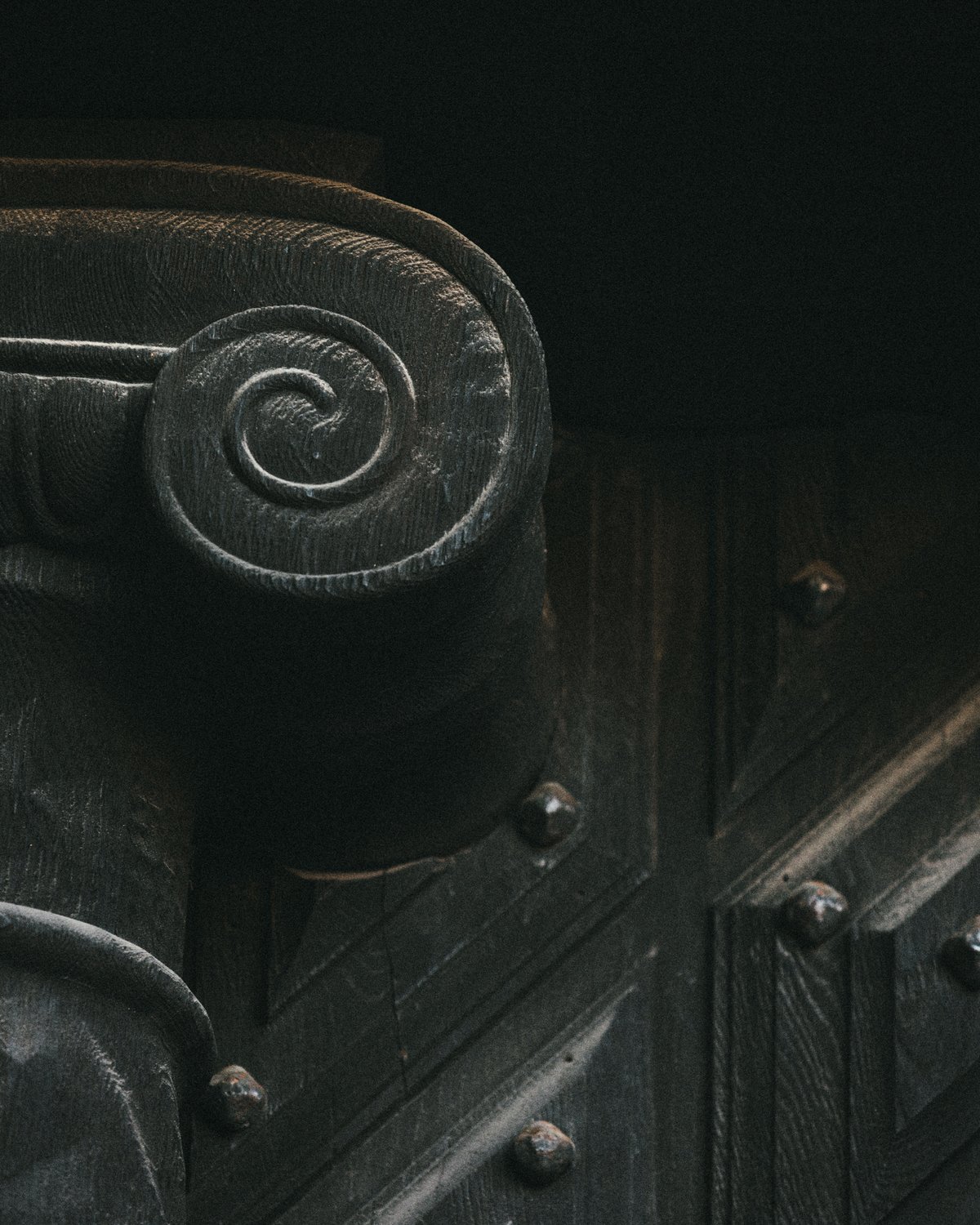 Close-up of a carved wooden Ionic column capital with visible patina and rivet details, inside Stockholm Concert Hall.