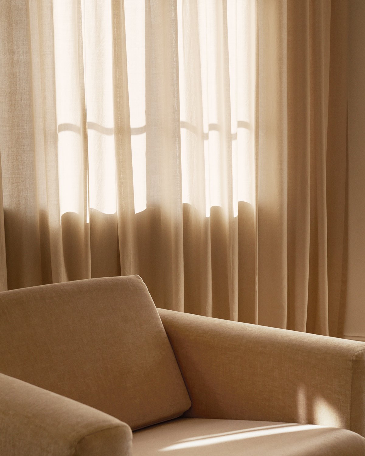 Close up shot of The Grand Pale Sand curtains by a soft armchair in Stockholm, Sweden.