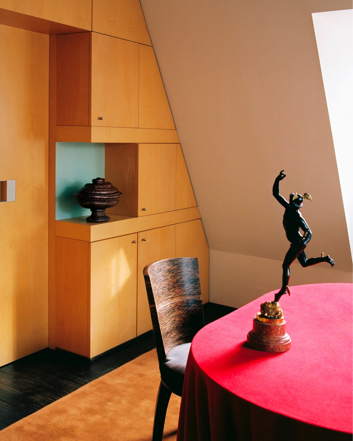 Grand in Pecan, photographed in warm light beneath a dining table with a red tablecloth, set against pale wood cabinetry.