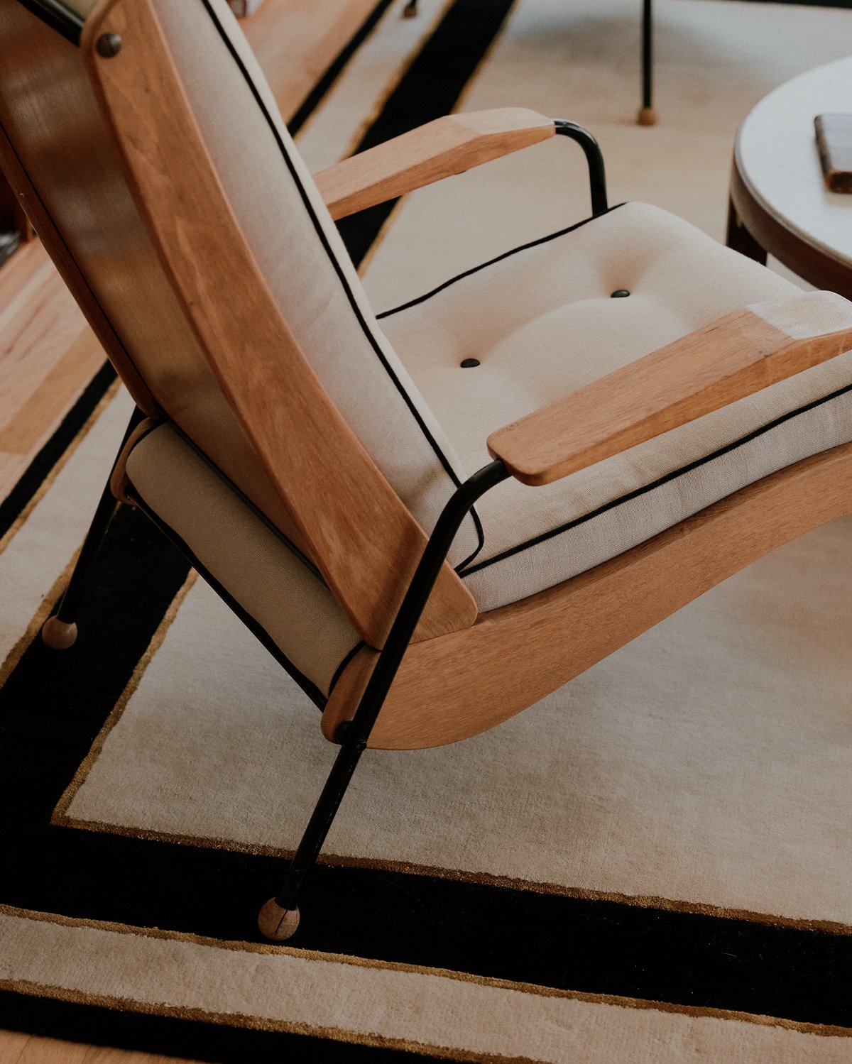 Gros plan du tapis en laine moelleuse Gild 01 avec un fauteuil blanc en bois.