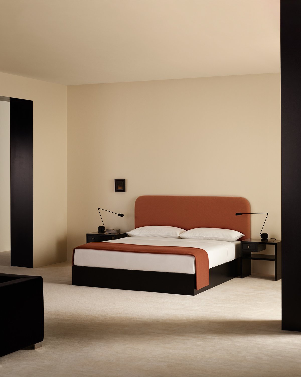 Heritage Throw in Rust, inszeniert auf einem Bett mit frischer weißer Bettwäsche und dem Signature Headboard in Burnt Red, fotografiert in einem minimalistischen Schlafzimmer mit schwarzen Nachttischen.