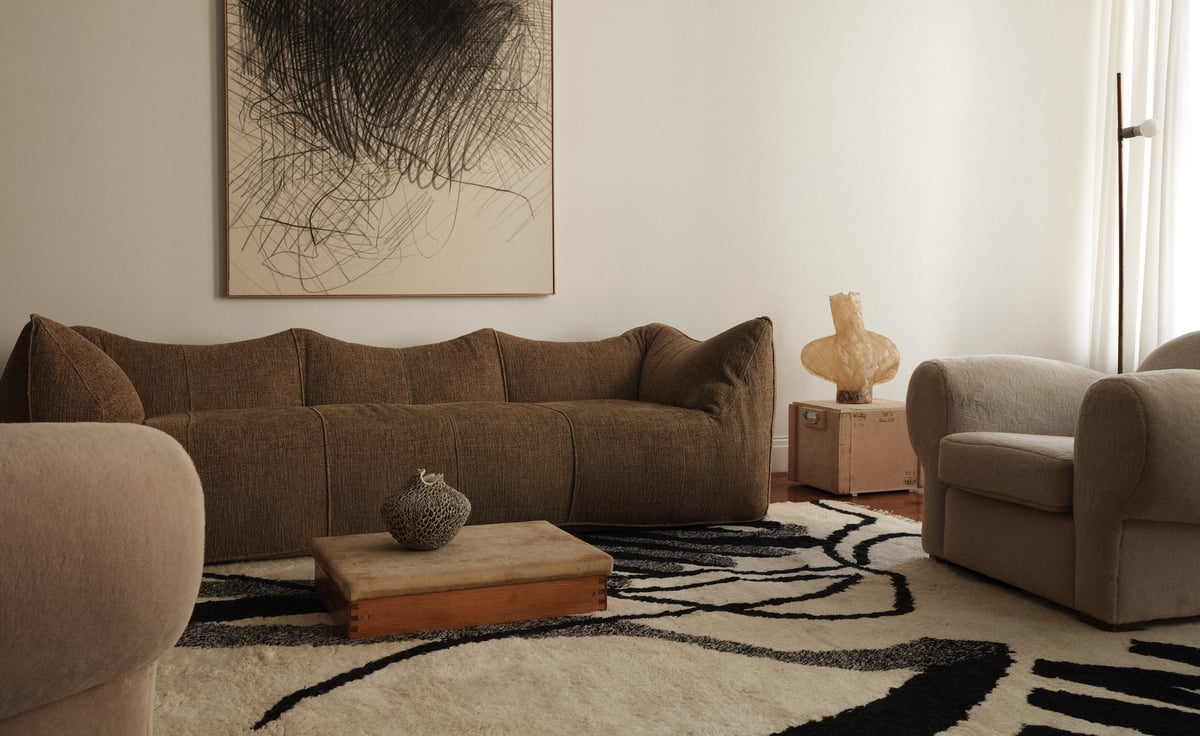 1212/21 von Aythamy Armas verankert den Raum mit kraftvoller, ausdrucksstarker Bewegung in Schwarz auf einem weichen elfenbeinfarbenen Grund. In Kombination mit einem tiefbraunen, strukturierten Sofa, skulpturaler Keramik und geschichteten Naturtönen setzt der Teppich einen grafischen Kontrast in einem sonst ruhigen, taktilen Interieur.