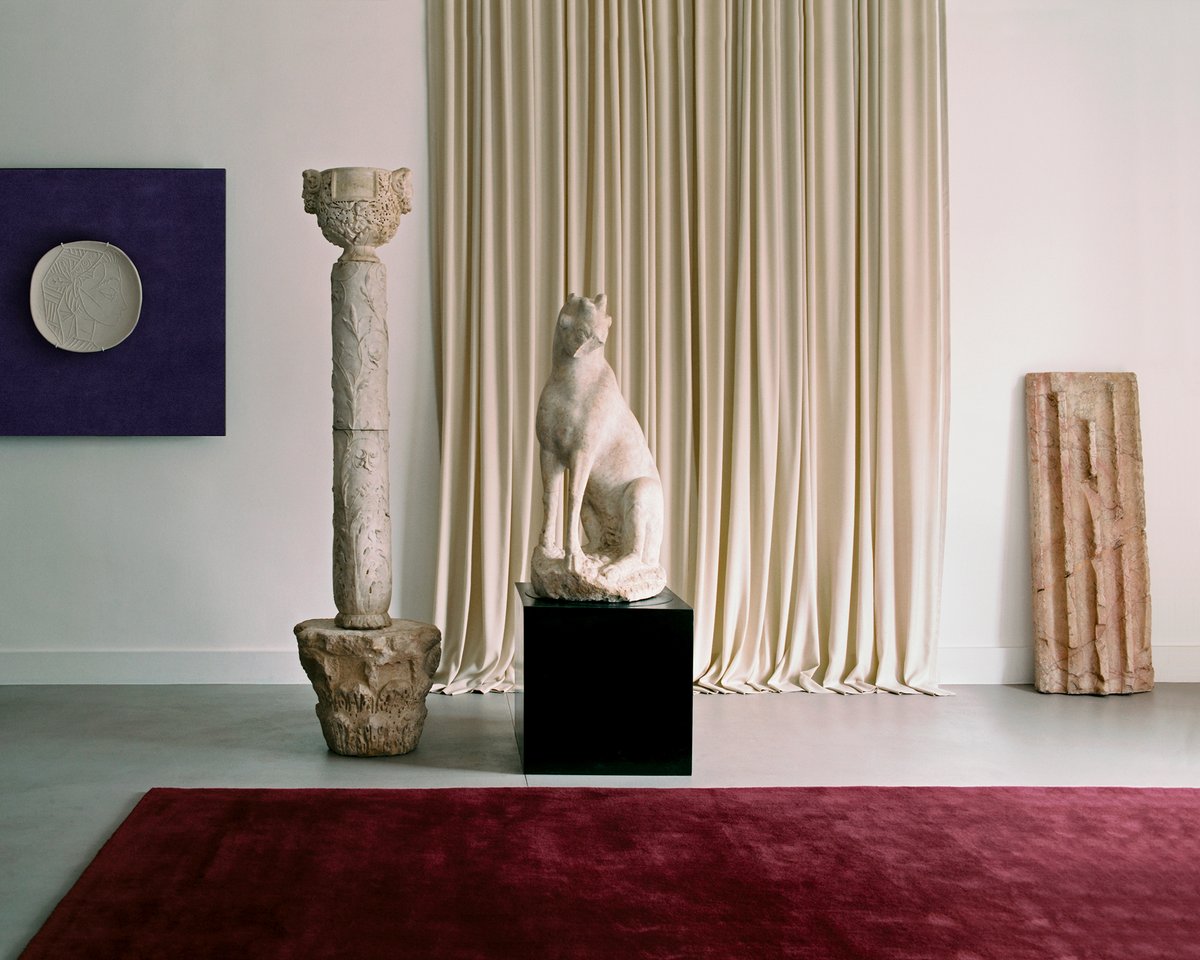 The Grand curtain in Pale Sand and the Grand rug in Deep Wine displayed in a room with sculptures, alongside a painting of the Grand rug in Lilac at Galerie Chenel in Paris.