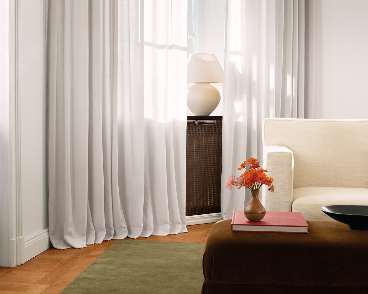 The Grand wool curtains in Soft Gray presented in a brightly lit living room next to the plush wool wug Grand in Moss.