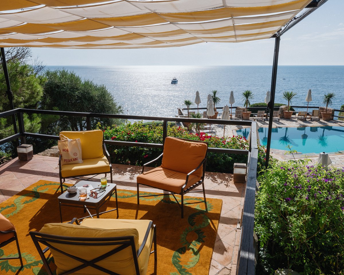 Climbing Vine ISSIMO rug pictured on a balcony with bushes overlooking a pool and the sea at the Hotel il Pellicano in Italy.