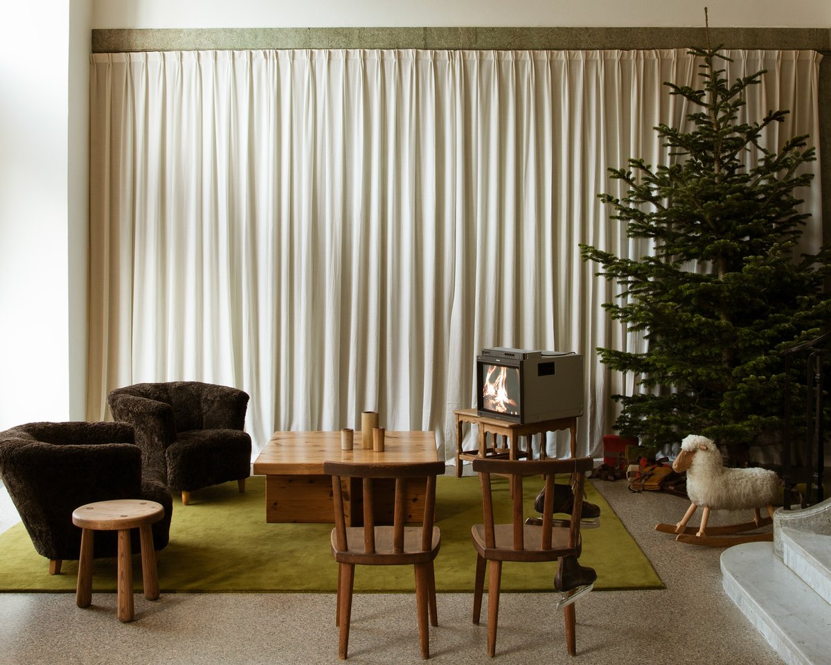 Grand Milano Green rug pictured in a living room with wooden furniture, The Grand Perfect White curtains, a TV, and a Christmas tree.