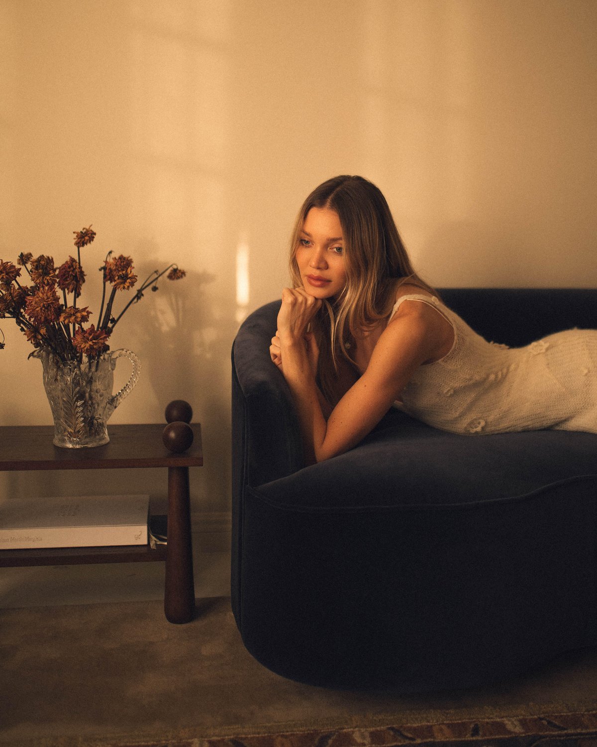Jessie Andrews photographed on a blue velvet sofa with the plush wool rug Grand - Chestnut underneath.