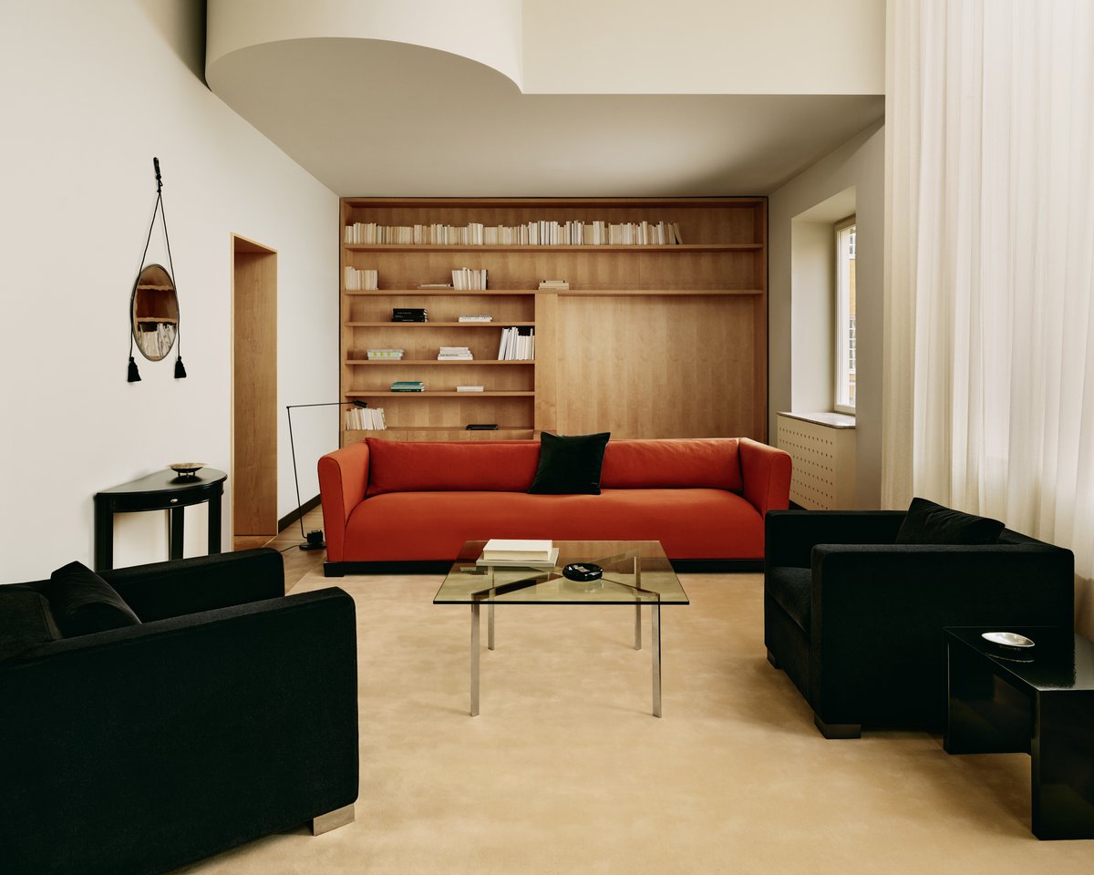 Grand rug in Butter displayed in a light living room with a vibrantly orange sofa, two black velvet chair and glas coffee table in Stockholm, Sweden.