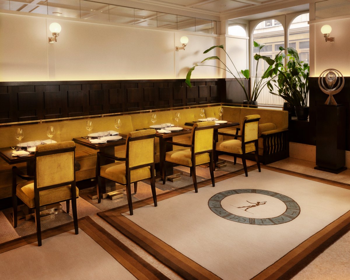 Plush wool rug Fabrizio Casiraghi - Astronomer depicted in a beautiful restaurant with large windows reflecting light onto yellow velvet furniture in Paris, France.