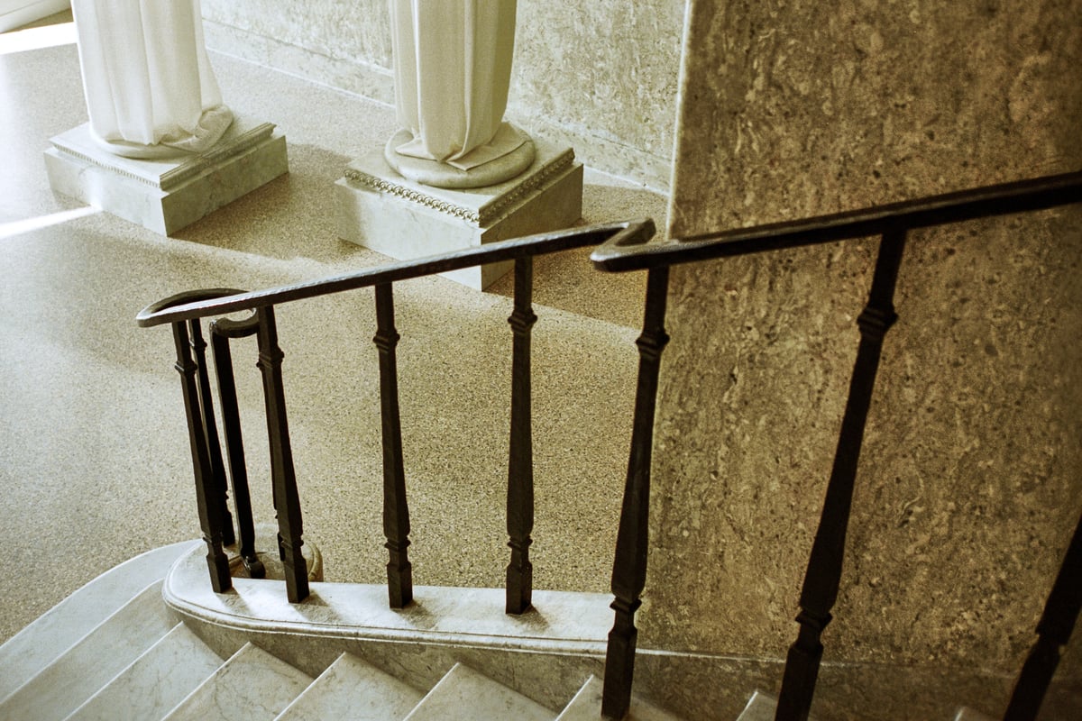 The marble detail walls and staircase looping down towards the Nordic Shade pillar exhibition in the Stockholm Flagship with the light shining in through the windows.