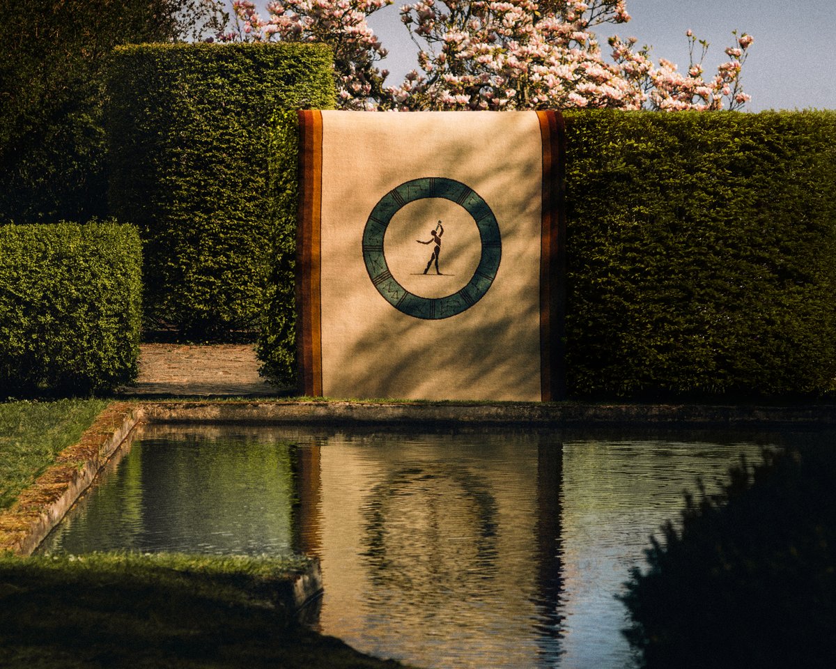 Behind a pond is the Fabrizio Casiraghi Astronomer rug draped over a hedge. Photographed in Sweden.