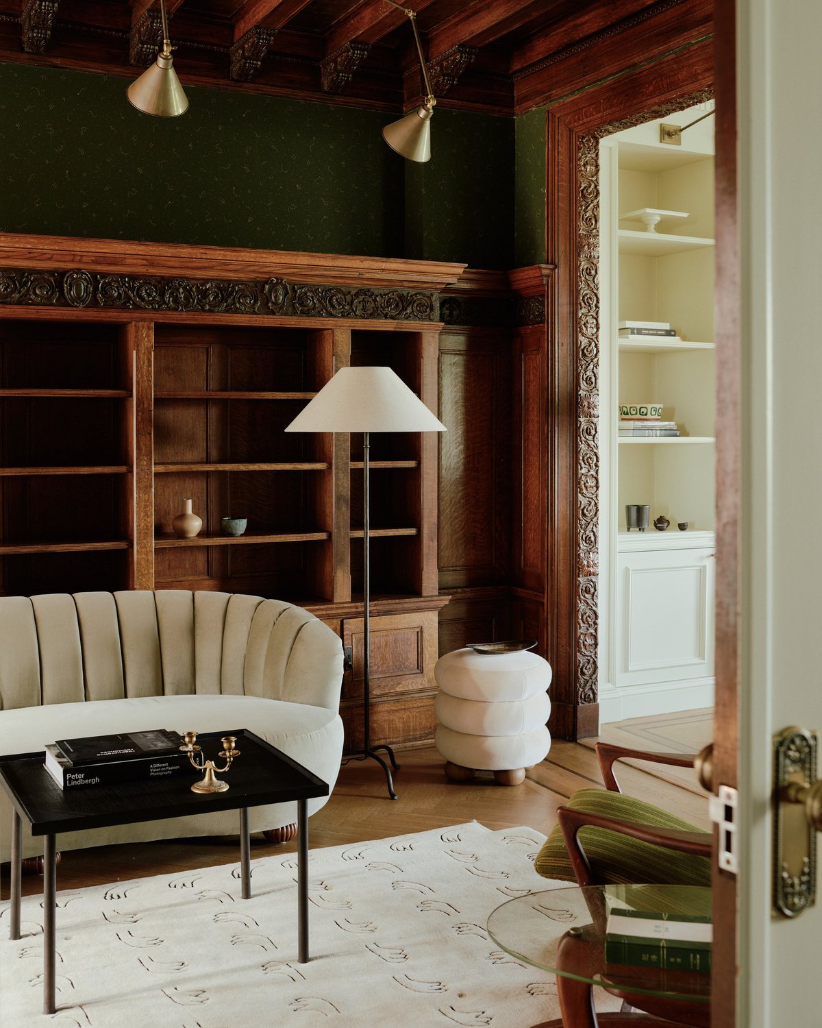 Flauschiger Wollteppich All Hands in hellem Beige abgebildet in einem gemütlichen Wohnzimmer mit einem weichen beigen Sofa, das im Kontrast zu einem großen Holzschrank und einer holzvertäfelten Decke steht.